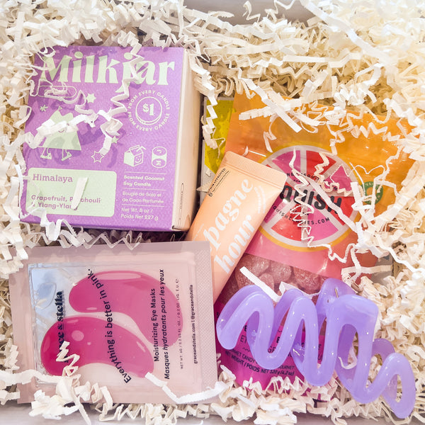 Gift box with skincare products including a purple box, pink packets, and a colorful bottle on a white background.