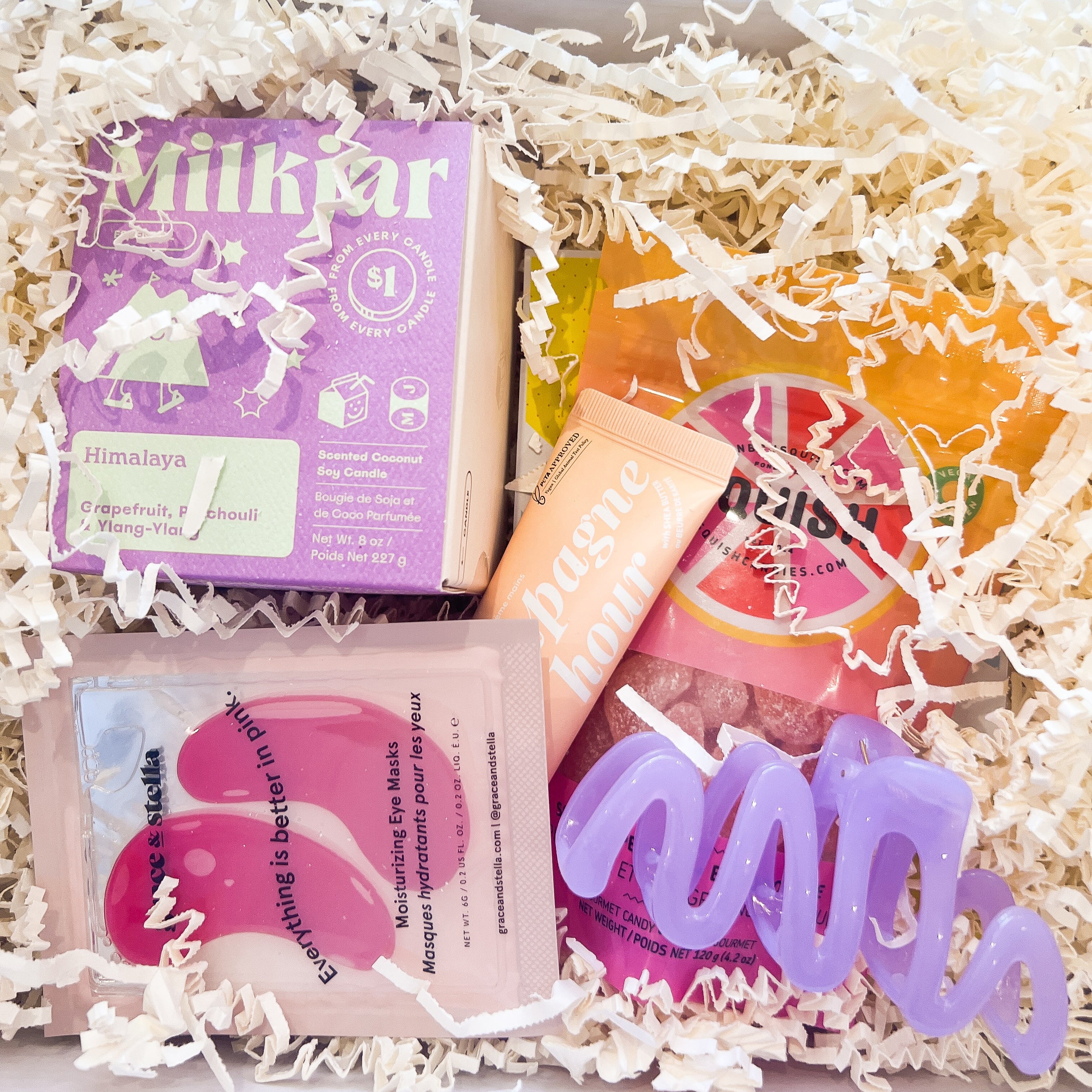 Gift box with skincare products including a purple box, pink packets, and a colorful bottle on a white background.